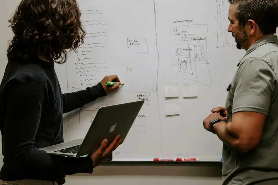 Person mapping a process on a whiteboard while a colleague holds a laptop